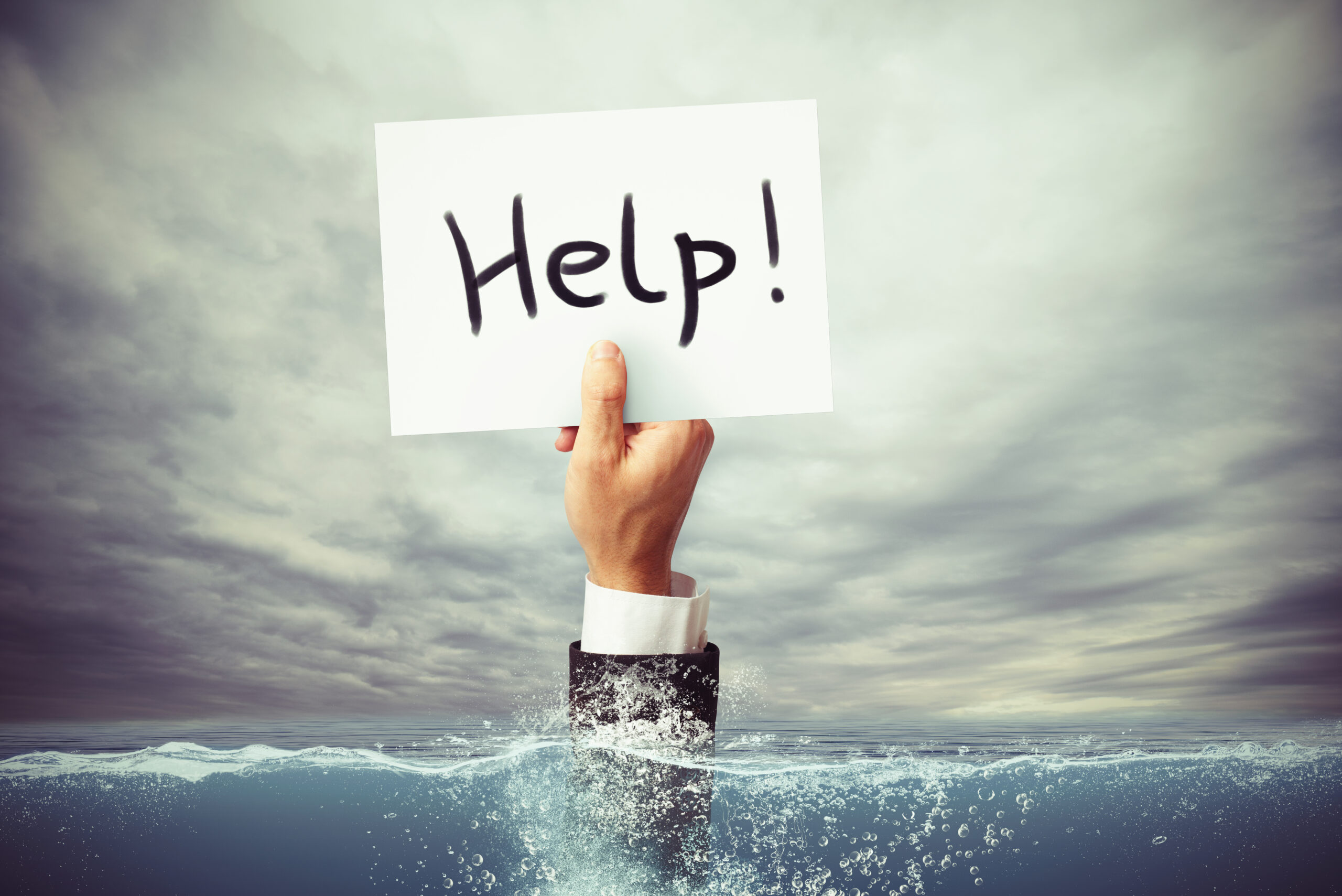 Businessman drowning in the sea with a hand holding a sheet of paper with help written